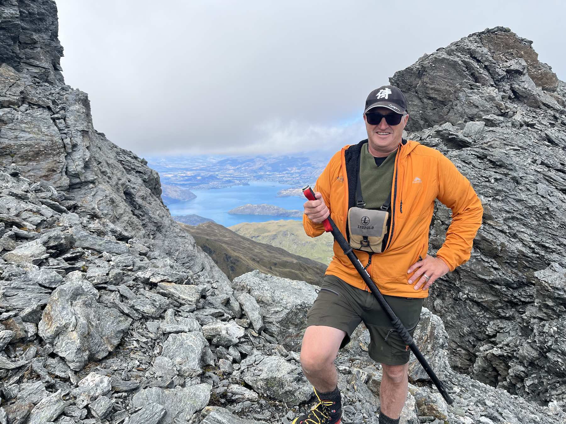 Orange jacket on rocky saddle with Stowt Staff